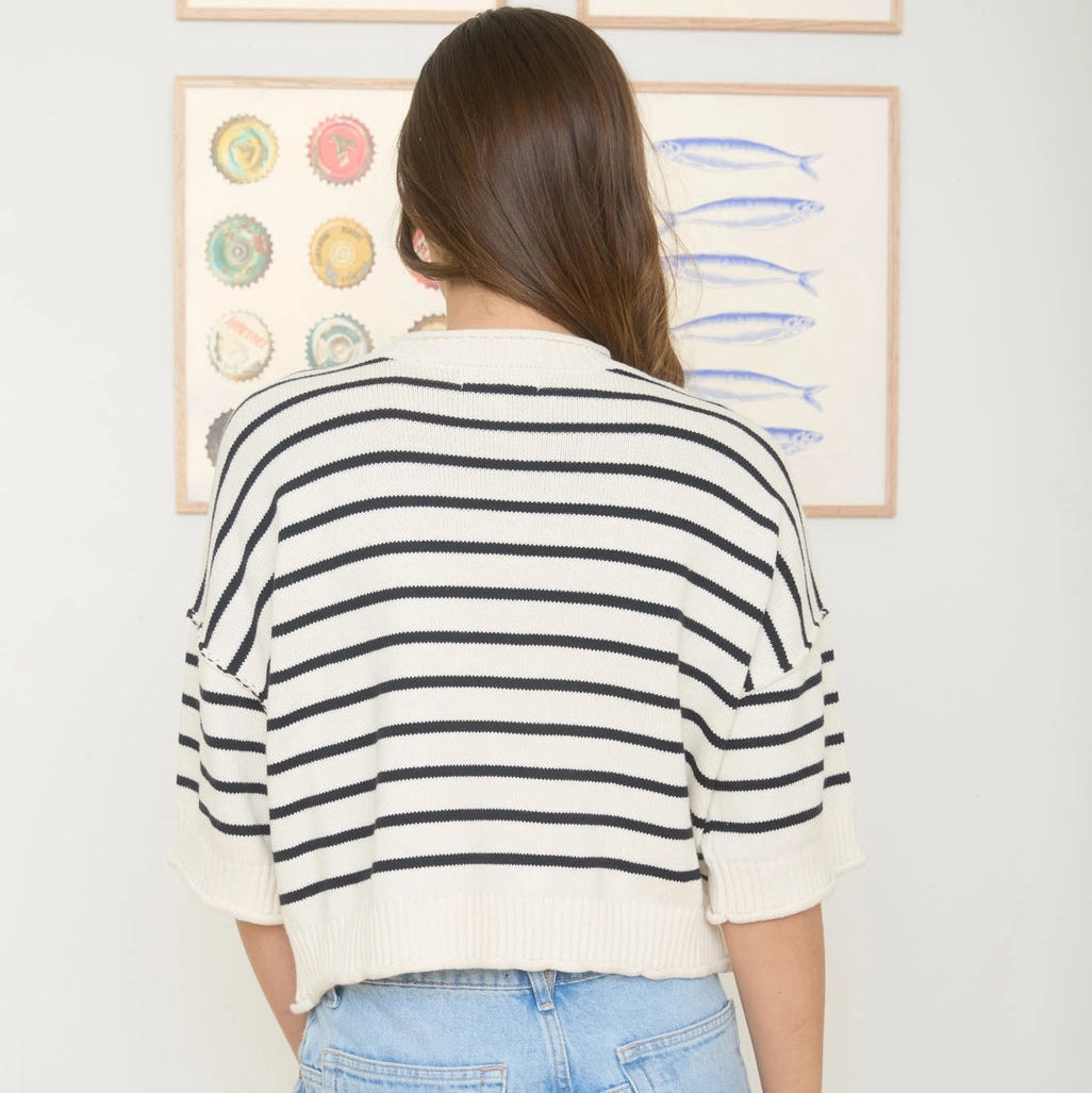 Person wearing a striped shirt and jeans standing in front of framed artwork on a wall.