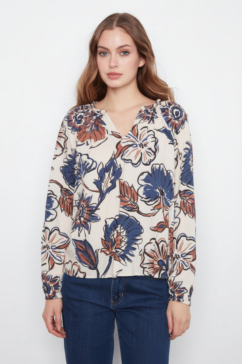 A woman wearing a long-sleeve V-neck blouse with a blue, brown, and white floral pattern, paired with dark blue jeans, against a plain white studio background.