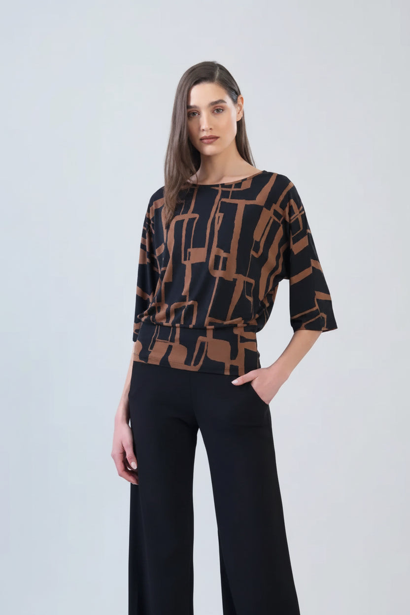 A woman modeling a black three-quarter sleeve top with a brown geometric line pattern, paired with black wide-leg trousers, against a light gray studio background.