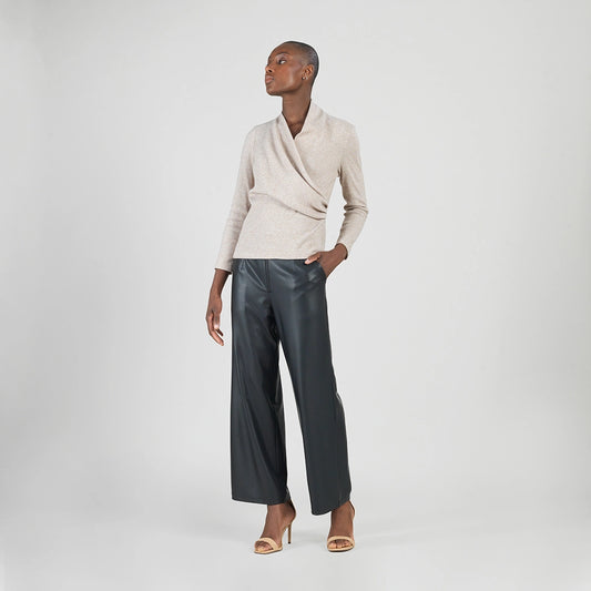 Person wearing a beige sweater and black pants on a white background