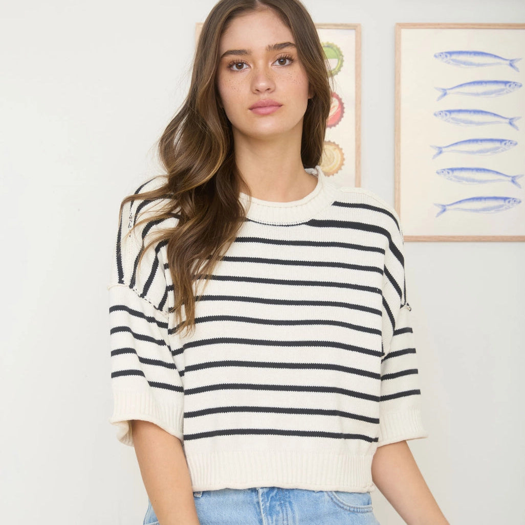 Woman wearing a striped shirt and jeans standing against a wall with framed pictures.