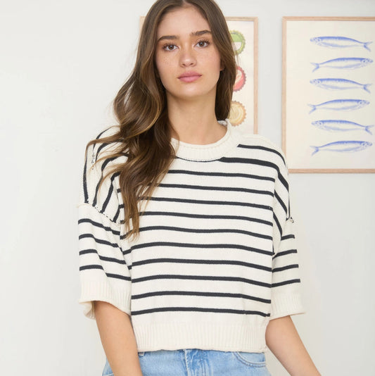 Woman wearing a striped shirt and jeans standing against a wall with framed pictures.
