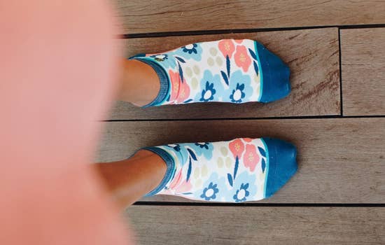 Ankle sock that say Earth Laughs in Flowers on the bottom. These blue, peach, line and white socks have colorful flowers on them.   Made of 58% Cotton, 22% Nylon, 16% Poly, 4% Spandex these are a nicely made, comfortable pair of socks. 