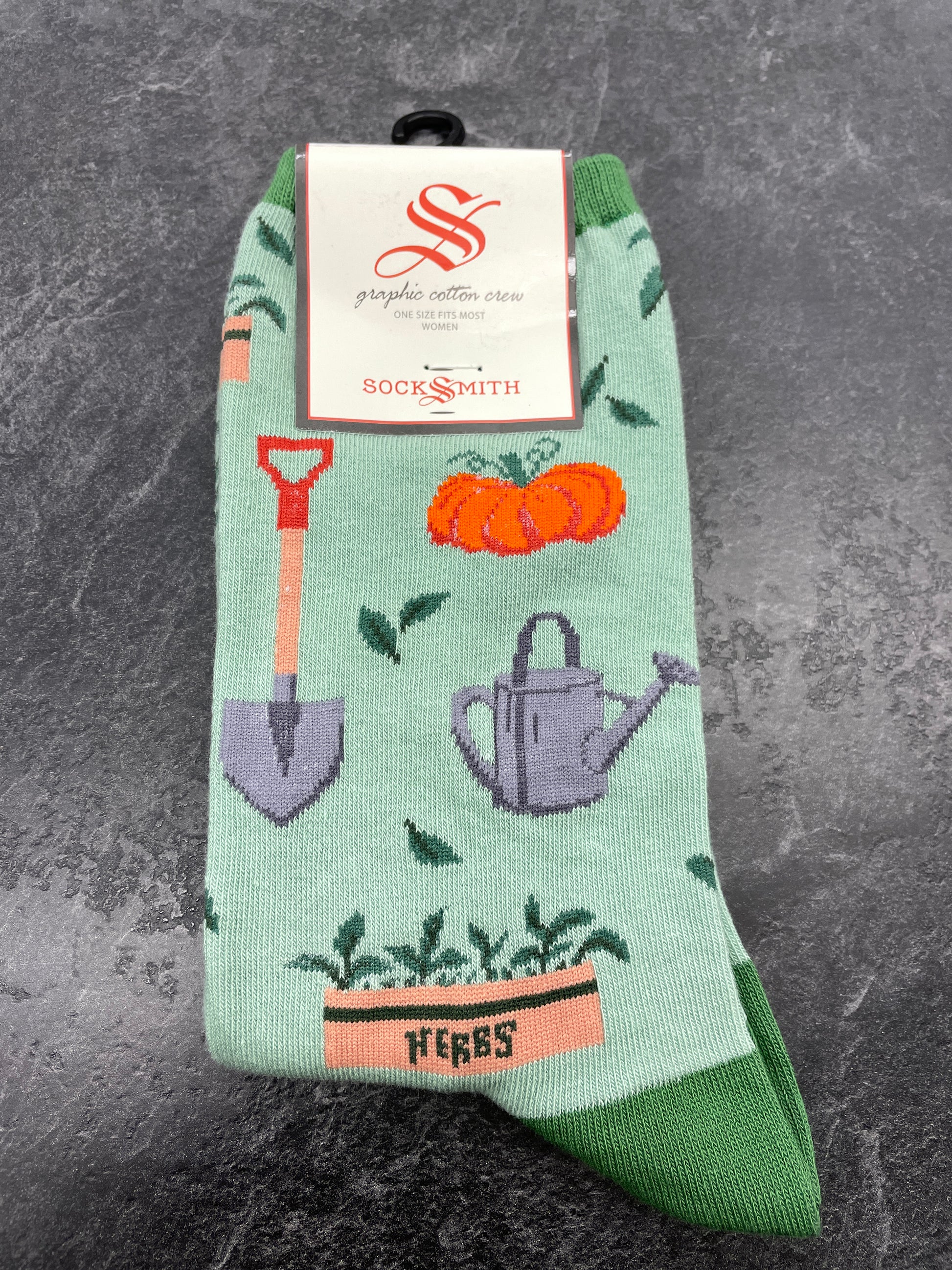 The happy gardener's sock has pictures of a shovel, watering can, herbs in a planter box, pumpkin and leaves. All on a light green background with green toe and heel. by Socksmith
